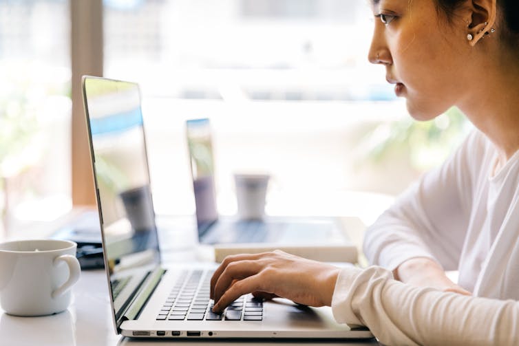 A woman sits at a desk using a laptop.