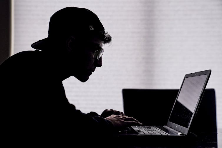 A person seen silhouetted sitting at a computer.