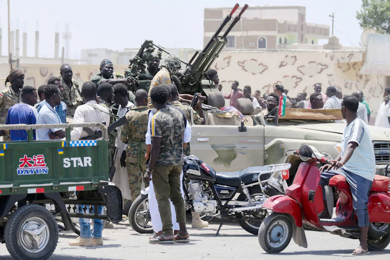 Men in fatigues sit in a vehicle with heavy machine guns.