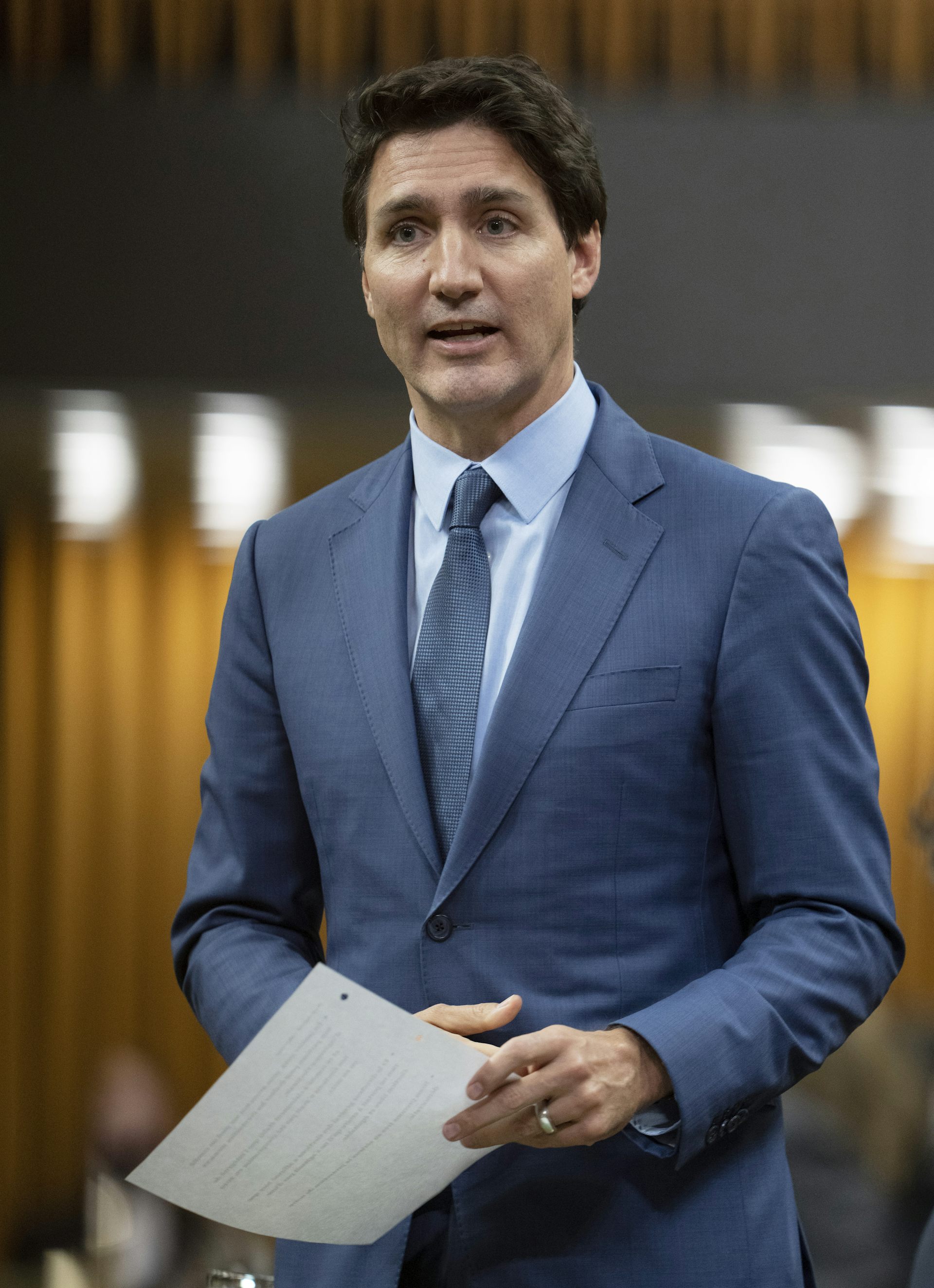 A man in blue suit speaking while holding a paper.