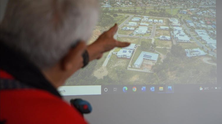 Older man gestures to aerial view of housing on projector screen.