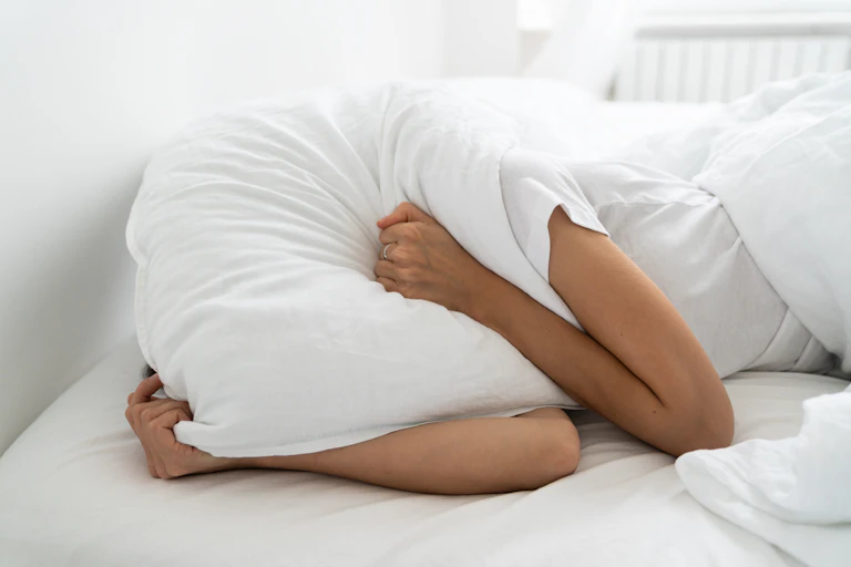 In bed with pillow over head.