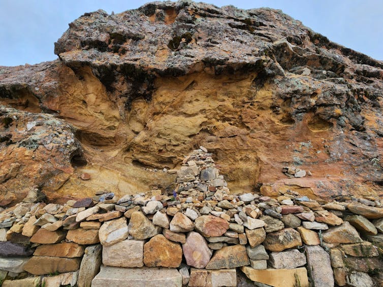 A small stack of stones sits before a sandy-colored hill.