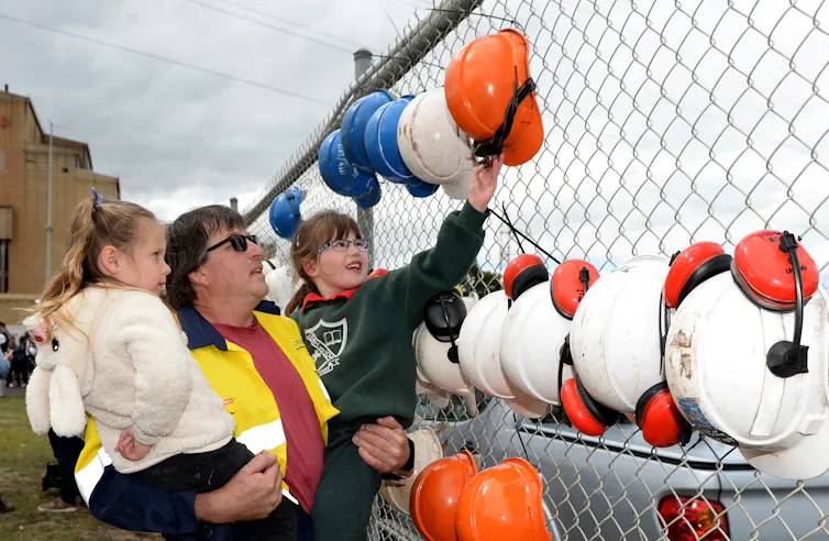 man shows children hard hats on fence