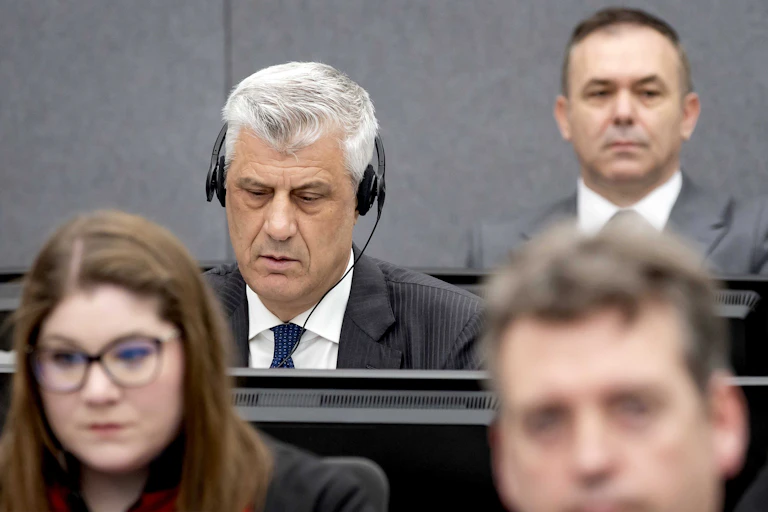 A group of people sit in the courtroom of The Hague, one listening to proceedings on headphones.