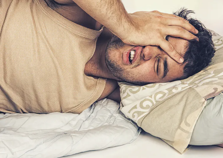 Young man in bed, rubbing face, trouble sleeping.