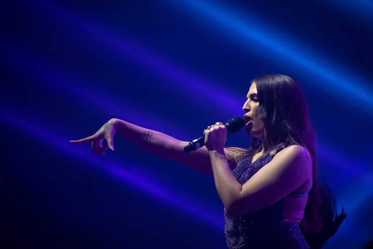 Mae Muller in profile, stretching out a hand as she sings.