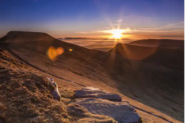 The sun appears over a vast mountain range.