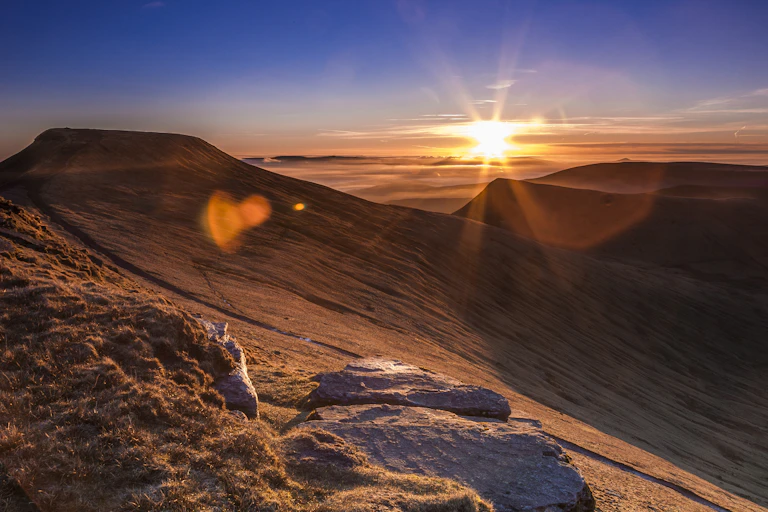 The sun appears over a vast mountain range.