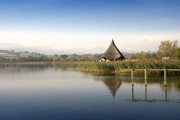 Mist hangs over a calm lake. On the other side of the shore is a triangular construction.