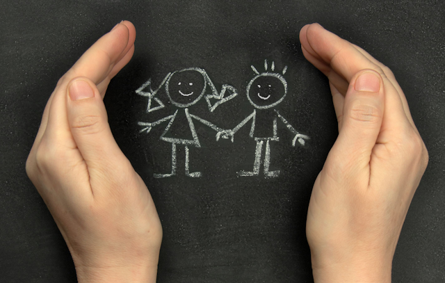 Chalk drawing of two children on a blackboard, with protective hands around them
