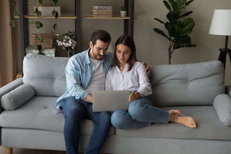 A man and a woman sitting on a sofa looking at a laptop screen together