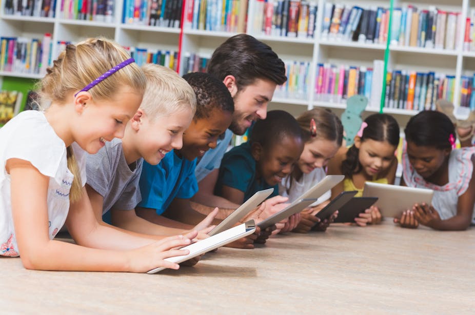 Des enfants et leur enseignant en train de lire sur des tablettes dans une bibliothèque
