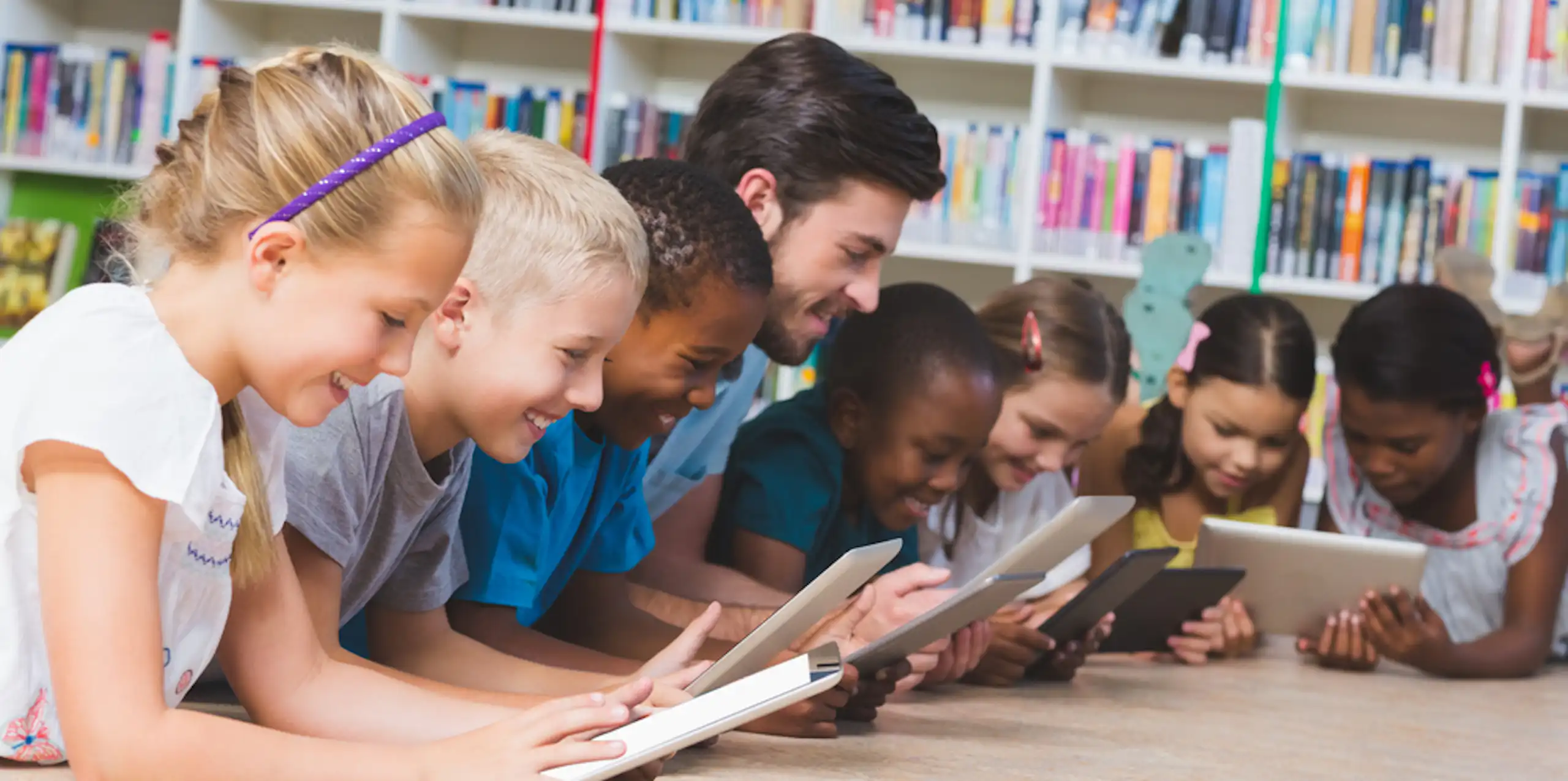 Des enfants et leur enseignant en train de lire sur des tablettes dans une bibliothèque