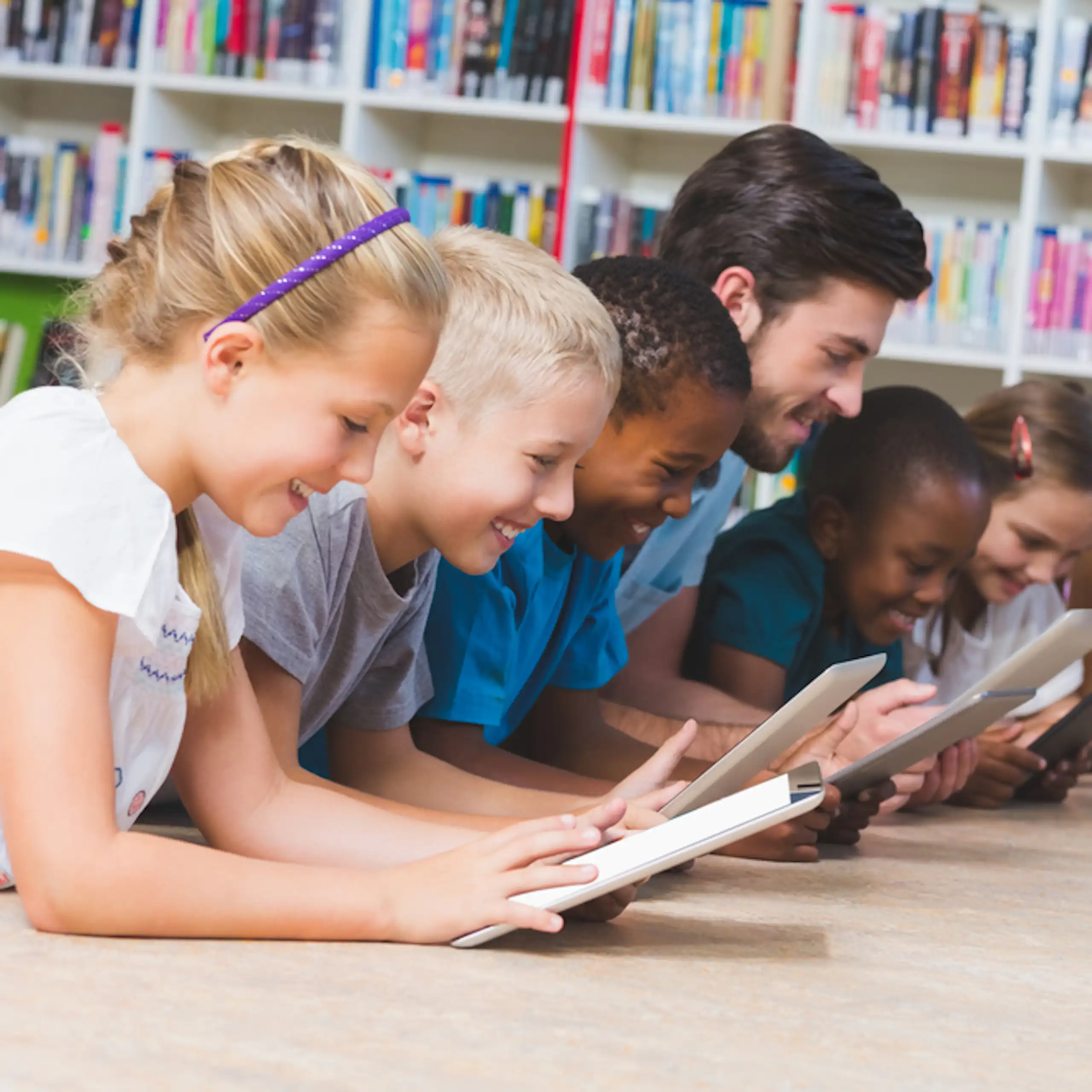 Des enfants et leur enseignant en train de lire sur des tablettes dans une bibliothèque