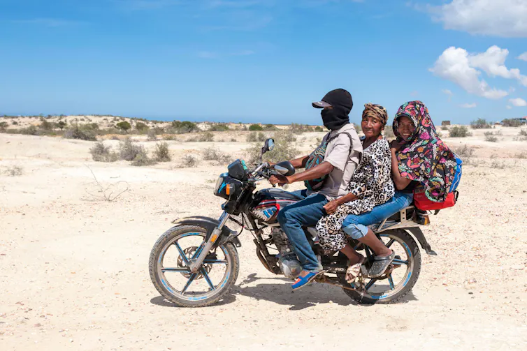 Three people sit on a motorbike.