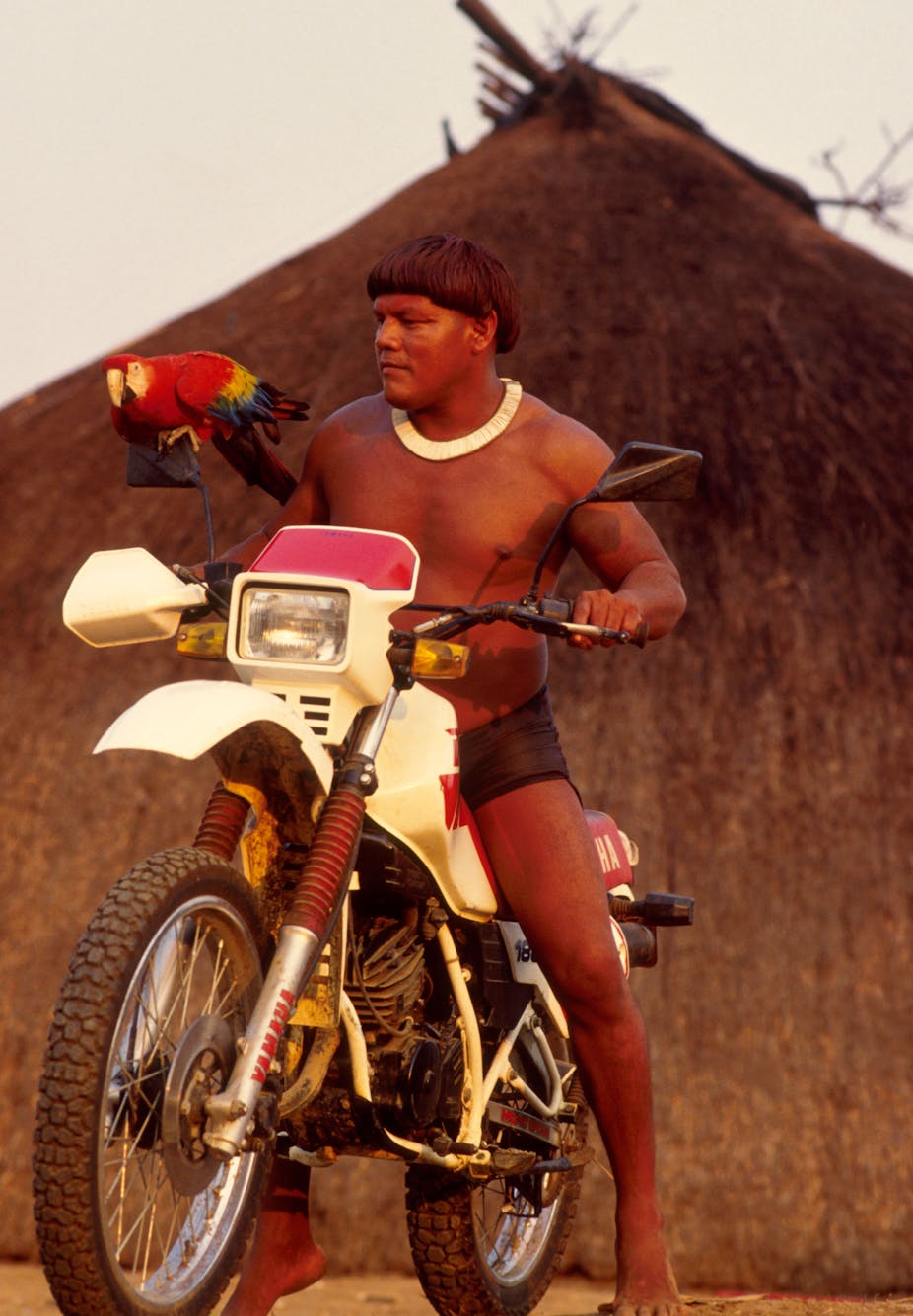 Indigenous man on motorbike with parrot.