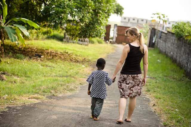 Young white woman walking hand in hand with African child.