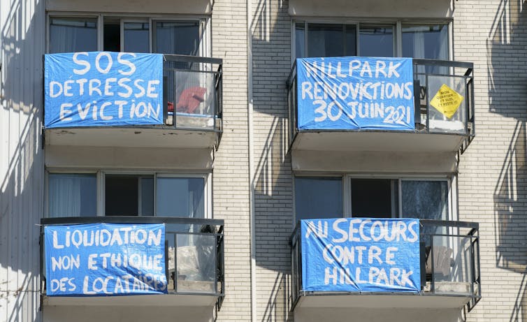 Four light blue banners with anti-eviction slogans written on them hang from apartment balconies.