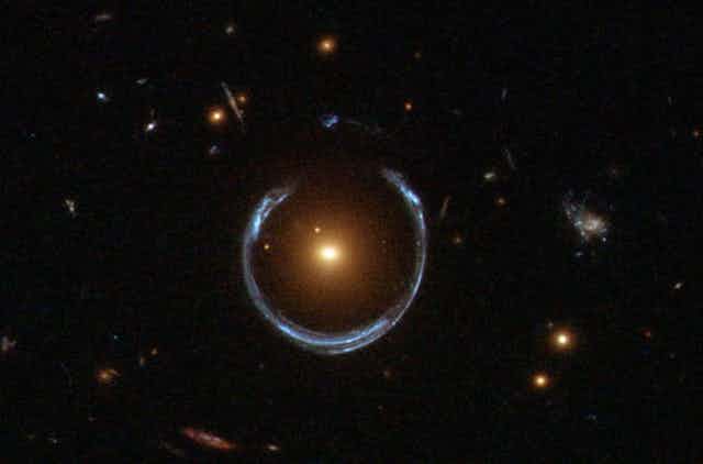 A photo showing an 'Einstein ring' of light around a bright central galaxy.
