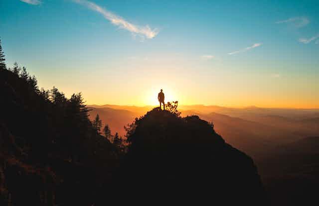 Person standing on a silhouetted hilltop at sunset