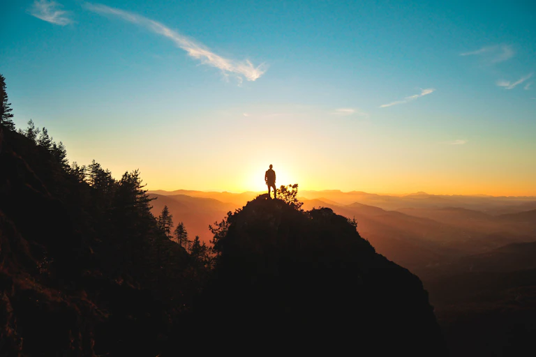Person standing on a silhouetted hilltop at sunset
