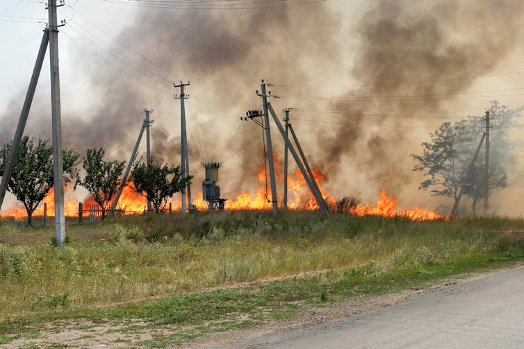 A wildfire encroaching on power lines in a field.