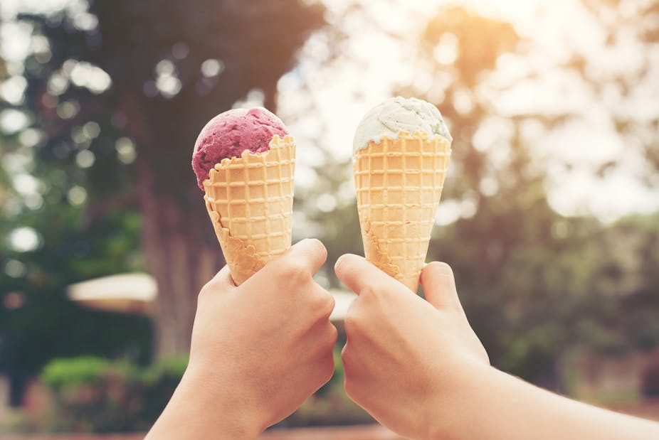 Two hands hold ice cream cones outside.