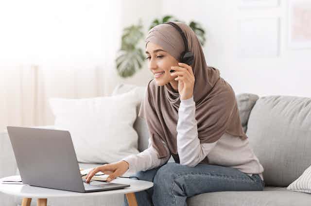 Young Arab woman at her laptop and speaking on a mobile phone.