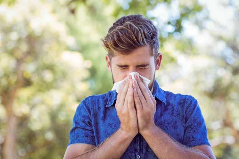 A young man outdoors blows his nose.