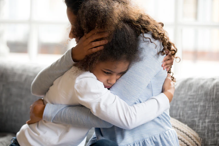 Mother hugging daughter on sofa