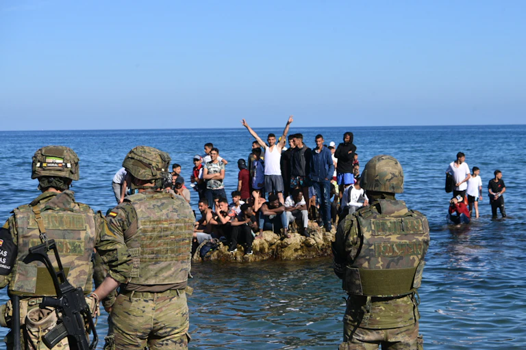 Soldats de dos, faisant face à un groupe de jeunes hommes juchés sur un rocher dans la mer