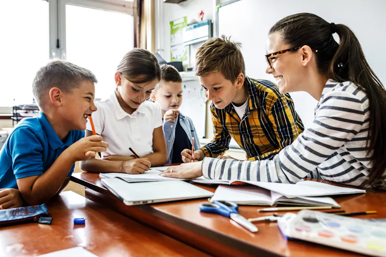 Une enseignante aide les élèves à terminer leur cours. Ils sont assis tous ensemble à un bureau