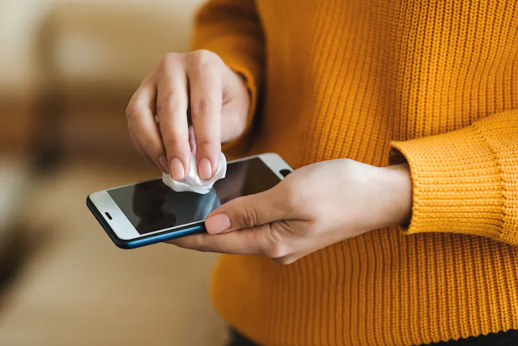 Mujer con jersey amarillo limpiando la pantalla del teléfono con una toallita.