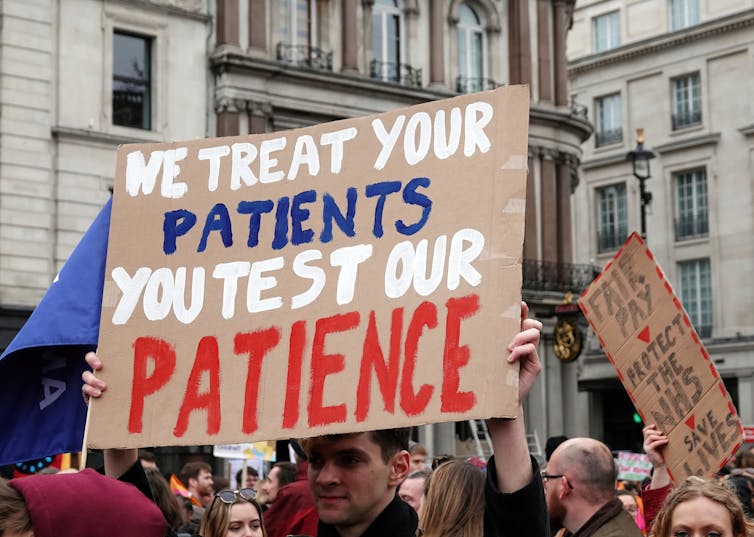 Man holds sign: 'we treat your patients you test our patience'