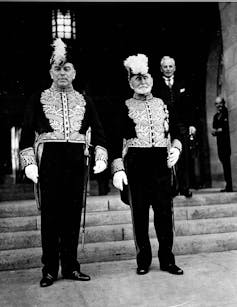 A black and white photo shows two men, one with a white beard, in military attire.