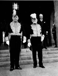 A black and white photo shows two men, one with a white beard, in military attire.