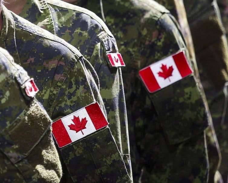 Shoulders of soldiers are seen with the Canadian flag sewn on their camouflaged jackets.