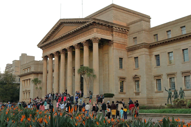 People standing on the steps in front of a big brown building.