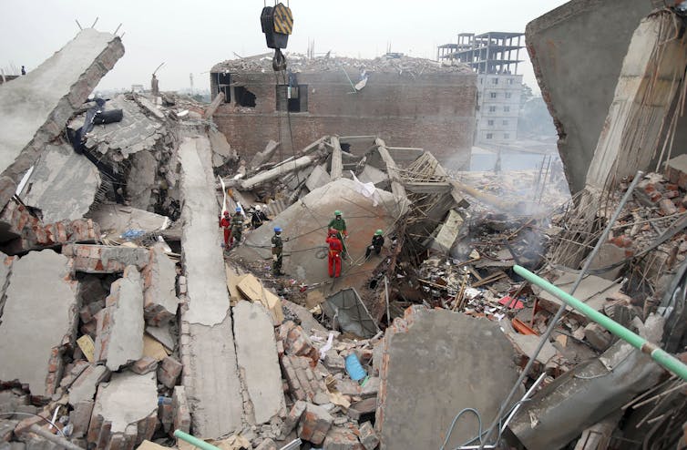 Uniformed rescue workers stand on top of a slab on top of a collapsed cement building.