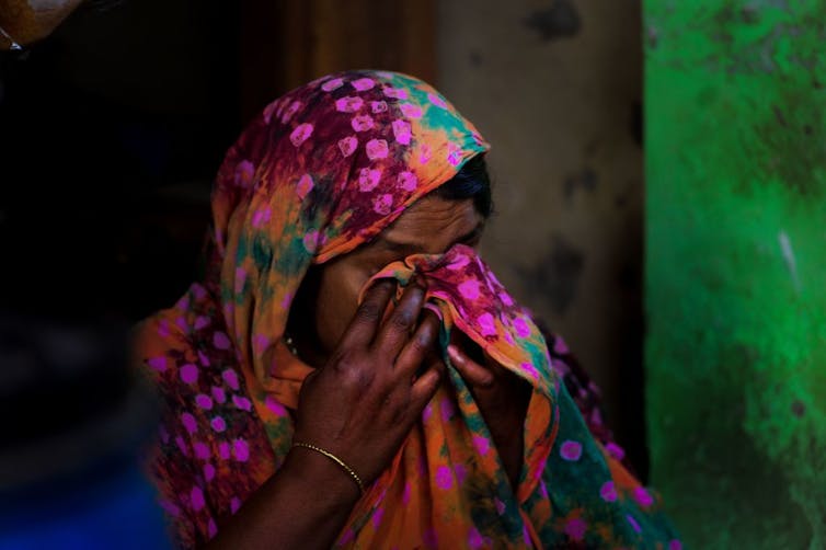 A woman cries, her face hidden in her brightly colored headscarf.