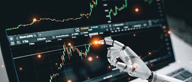 Robot arm touching financial chart on a laptop screen.