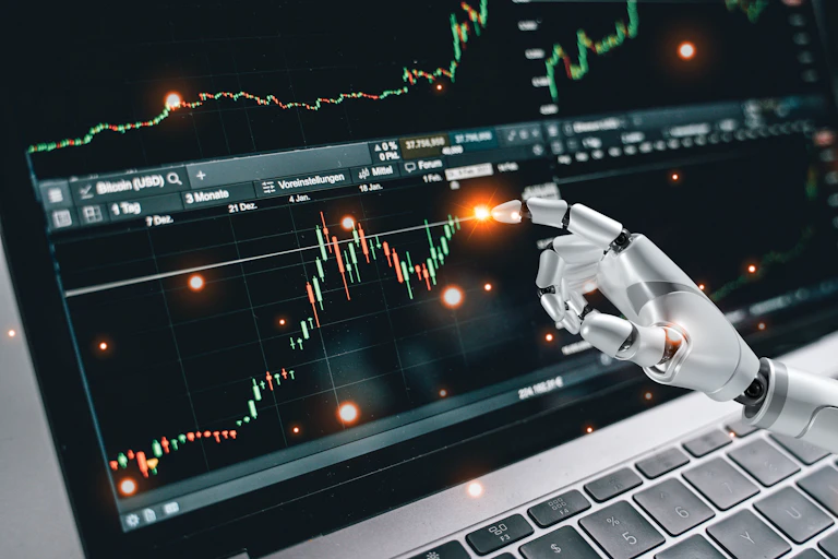 Robot arm touching financial chart on a laptop screen.