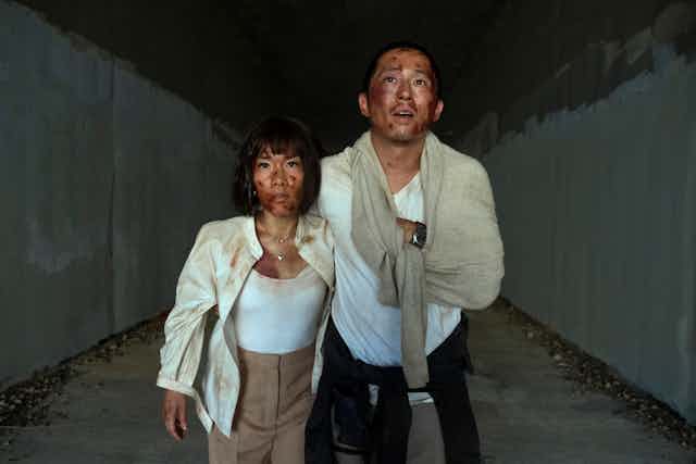 Two badly beaten up people walking down a tunnel.