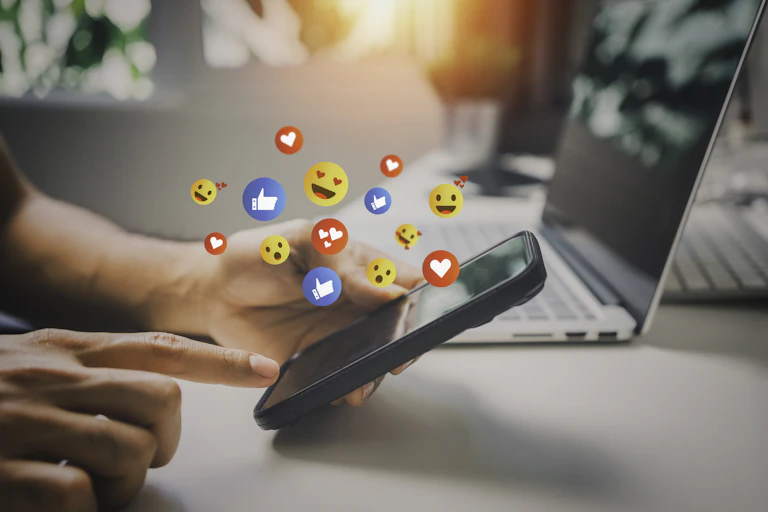 Person scrolls on phone while heart, thumbs up and other emojis float above screen