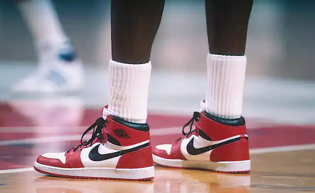 Legs of basketball player wearing red, black and white hightop sneakers.