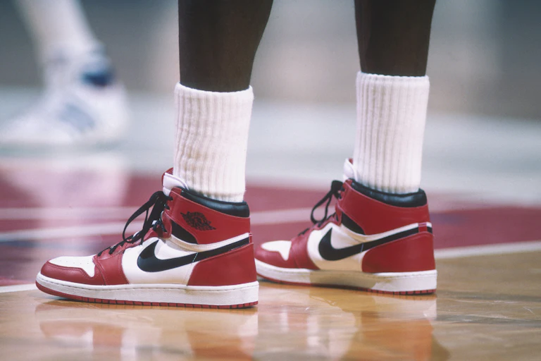 Legs of basketball player wearing red, black and white hightop sneakers.