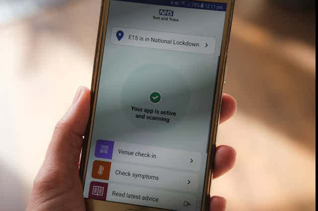 A hand holds a smartphone displaying the NHS COVID app.