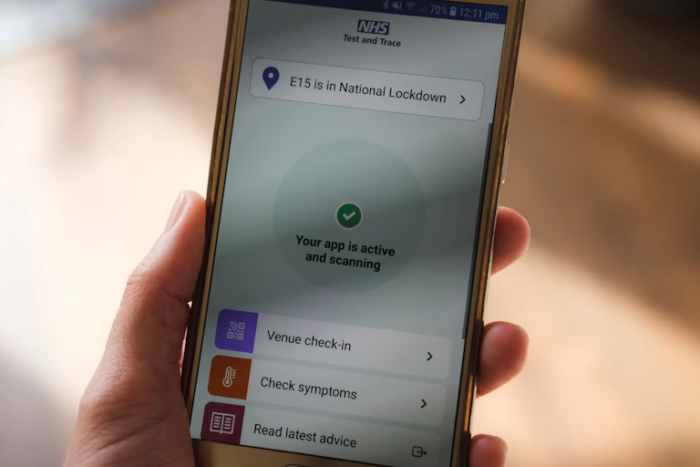 A hand holds a smartphone displaying the NHS COVID app.