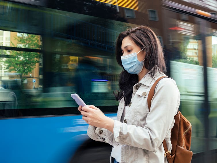 A woman wearing a mask looks at her phone.